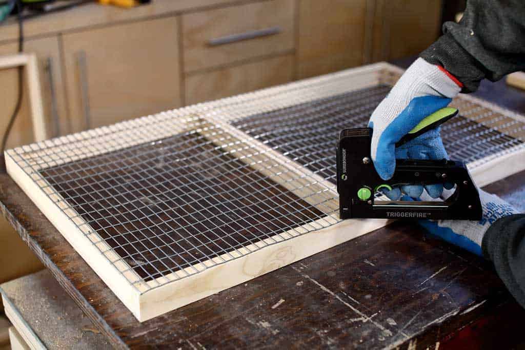 stapling wire mesh screen to floor frame of DIY rabbit hutch